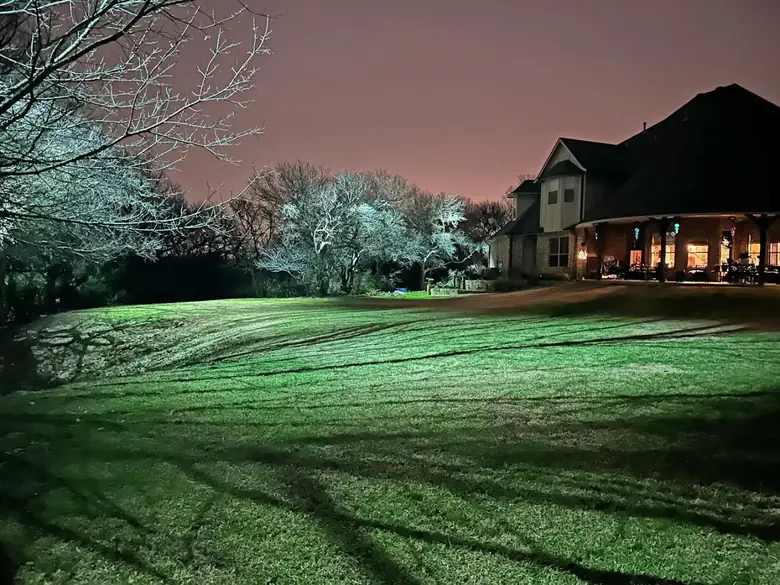 Estate lawn in Argyle, Texas with moonlit bare trees and a warmly lit covered porch beyond