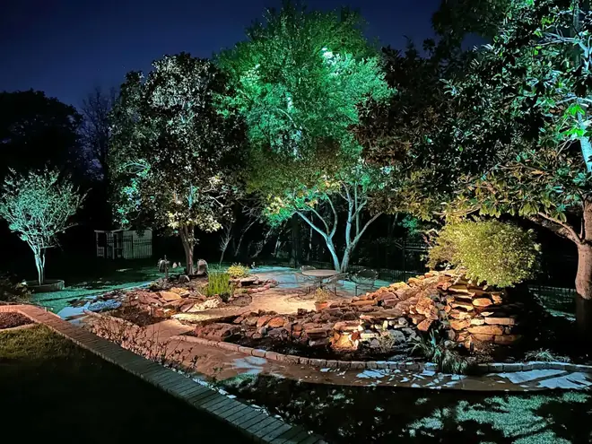 Colleyville, Texas back garden at night with a lit rock waterfall, flagstone patio and uplit magnolias