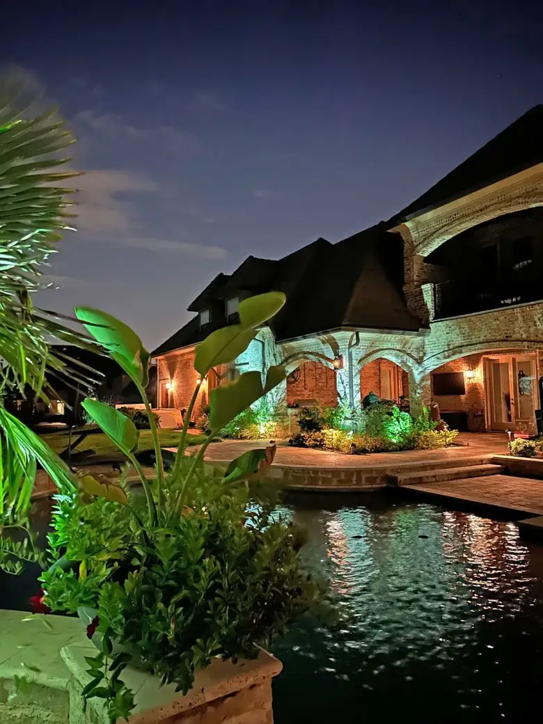 Brick home in Dallas, Texas reflected in a lit pool with tropical planting in the foreground