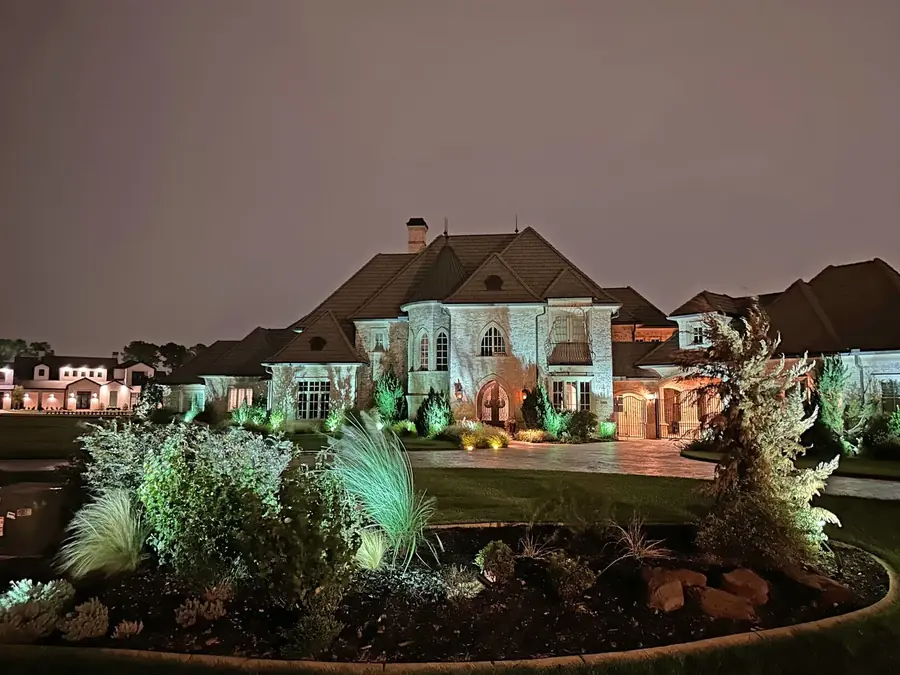 Stone Dallas, Texas estate at night with uplit ornamental grasses, shrub beds and a warmly lit motor court