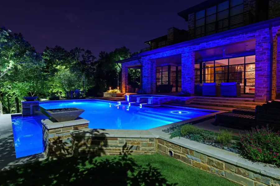 Modern stone home in Flower Mound, Texas at night with a blue-lit pool, spa spillway and color-washed stone columns