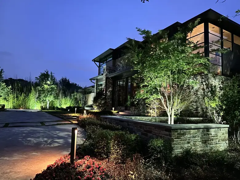 Modern stone and glass home at dusk in Flower Mound, Texas with bollard path lights and uplit ornamental trees